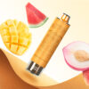 A vape device with a textured golden brown casing, surrounded by slices of watermelon, mango, and peach, set against a light yellow background.