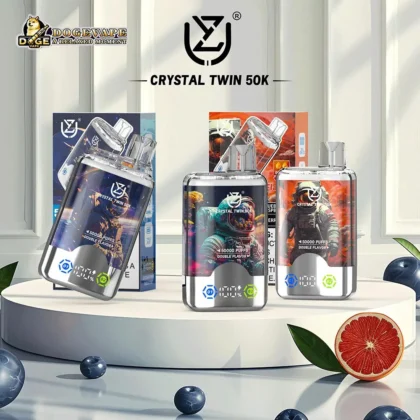 Three Crystal Twin 50K disposable vape devices featuring astronaut-themed designs and labeled with 50000 puffs and double flavor capability, displayed on a white pedestal surrounded by fruit and decor elements.