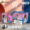 Product display of UZY Triple Flavor disposable vape with 6000 puffs, showing pink and blue device, packaging boxes with monkey character designs, flavor details (Peach Mango Pineapple, Blue Razz Ice, Raspberry Watermelon), icons for triple mesh coil, 54ml, 850mAh battery, and Type-C port, set against geometric backdrop with soft lighting